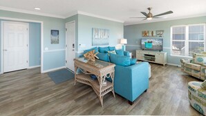 Un salon avec un canapé bleu, une table d’appoint en osier et un ventilateur de plafond.