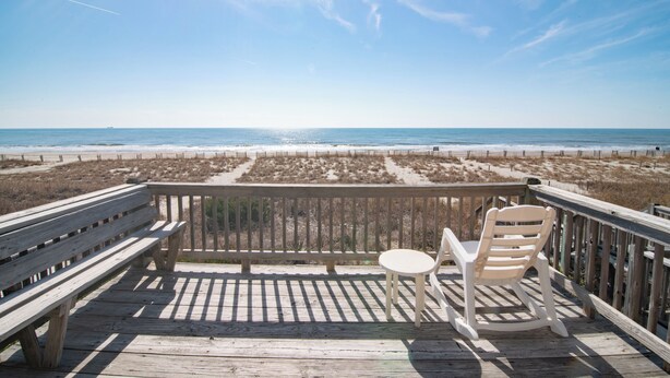 Une terrasse en bois avec un banc et un fauteuil à bascule donnant sur une plage.