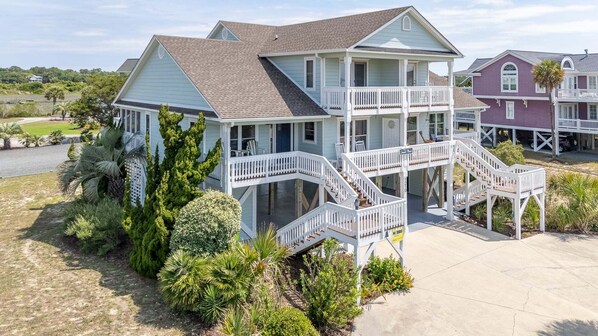 A two-story beachfront house with a balcony and a covered porch.