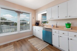A kitchen with white cabinets, a dishwasher, a coffee maker, and a green trash bin.