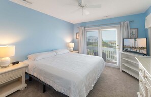A bedroom with a bed, nightstands, a TV, and a view of the outdoors through a window.