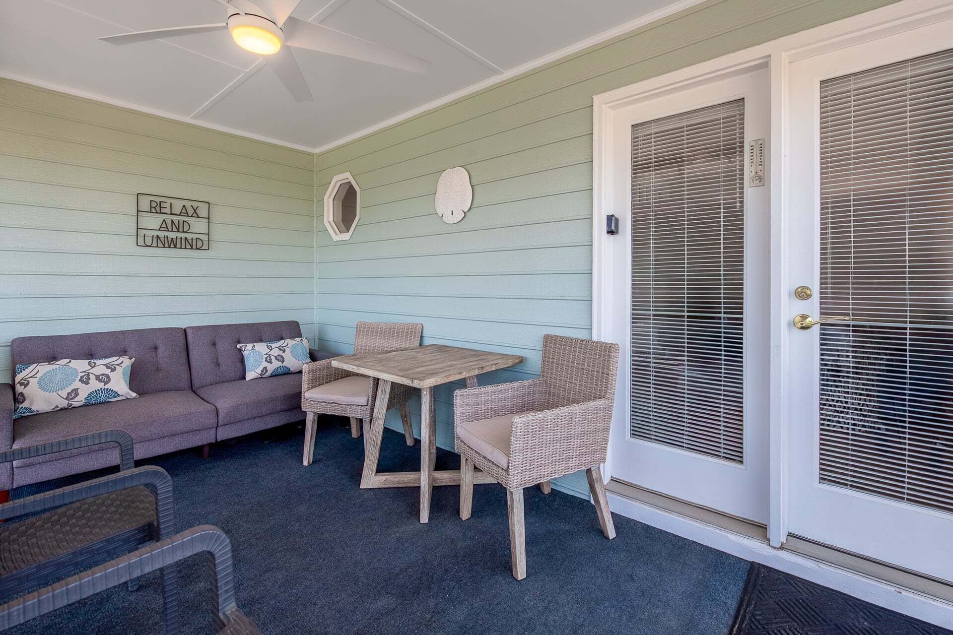A covered porch with a table and chairs, a sofa, and a door with blinds.