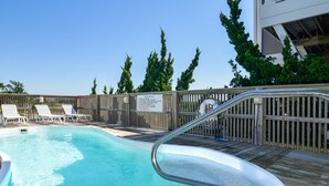 A swimming pool with a wooden deck, lounge chairs, and a fence. - Hobbs Realty - Oceanfront home w/Private Pool, Luggage Lift, and Hot Tub (Holden Beach)