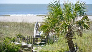 A beach with a palm tree and a wooden boardwalk. - Hobbs Realty - Oceanfront home w/Private Pool, Luggage Lift, and Hot Tub (Holden Beach)