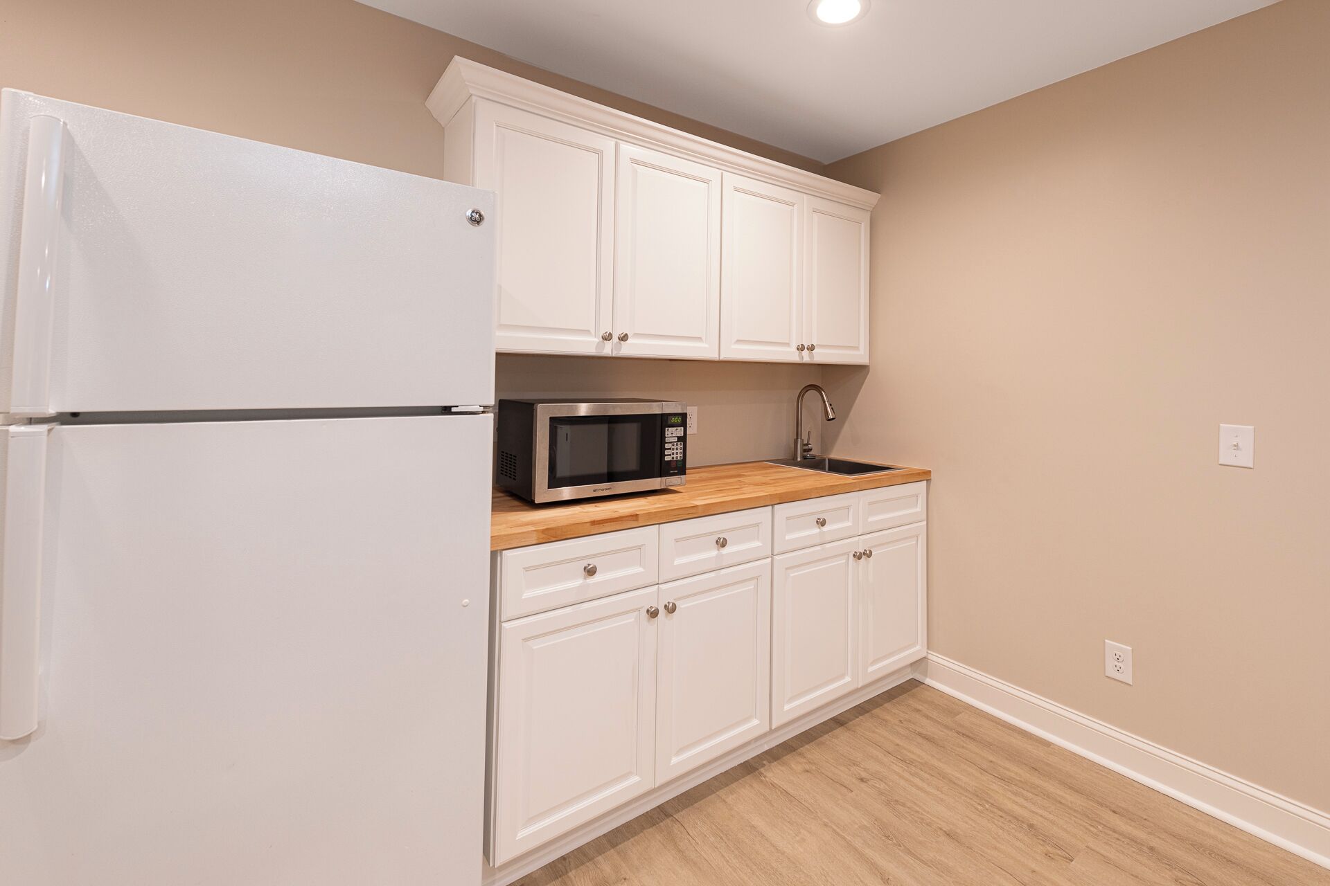 A compact kitchen with white cabinetry, a microwave, and a refrigerator.