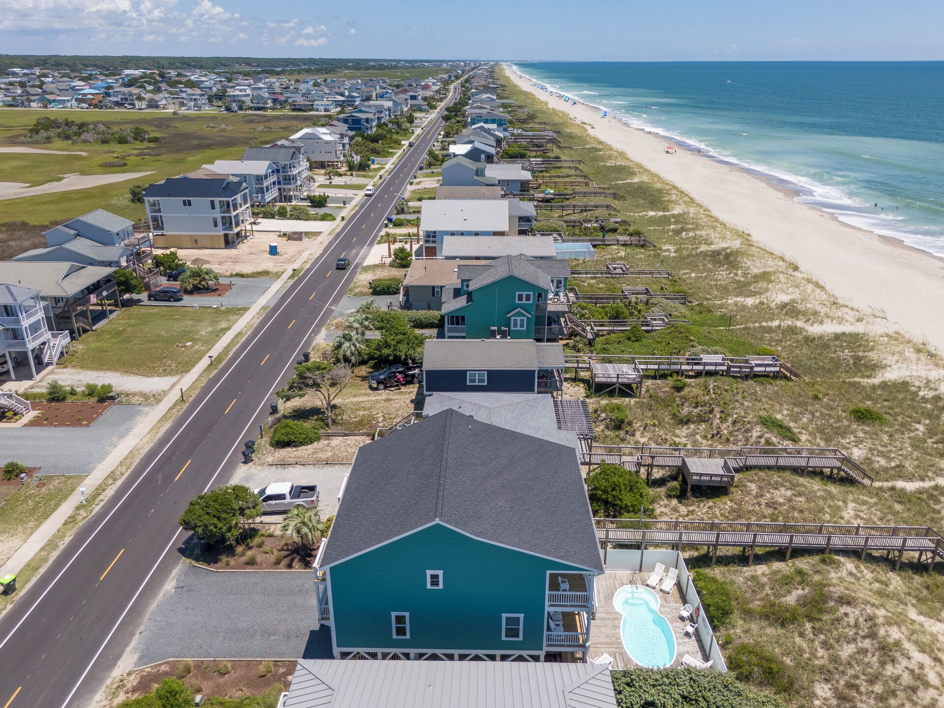 A coastal residential area with houses along a beach, a road, and a swimming pool.