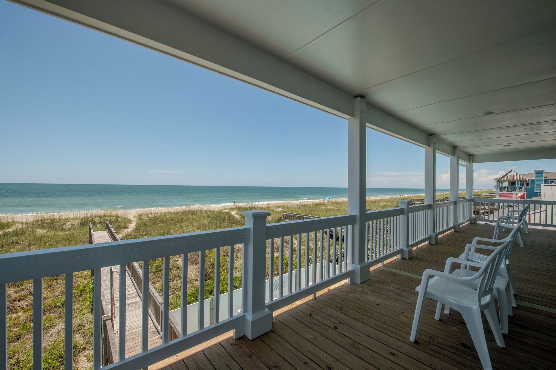 A covered deck with white railings overlooking a beach.