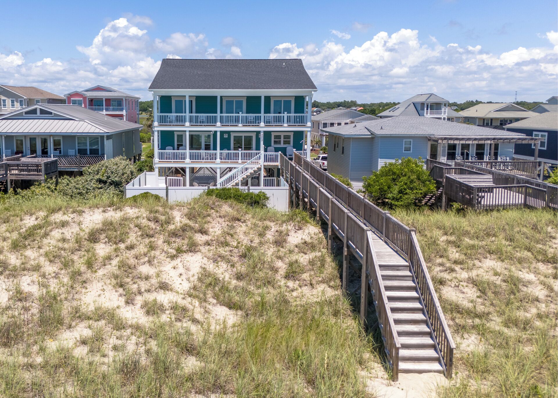 A beachfront property with a two-story house featuring a balcony and a wooden deck.