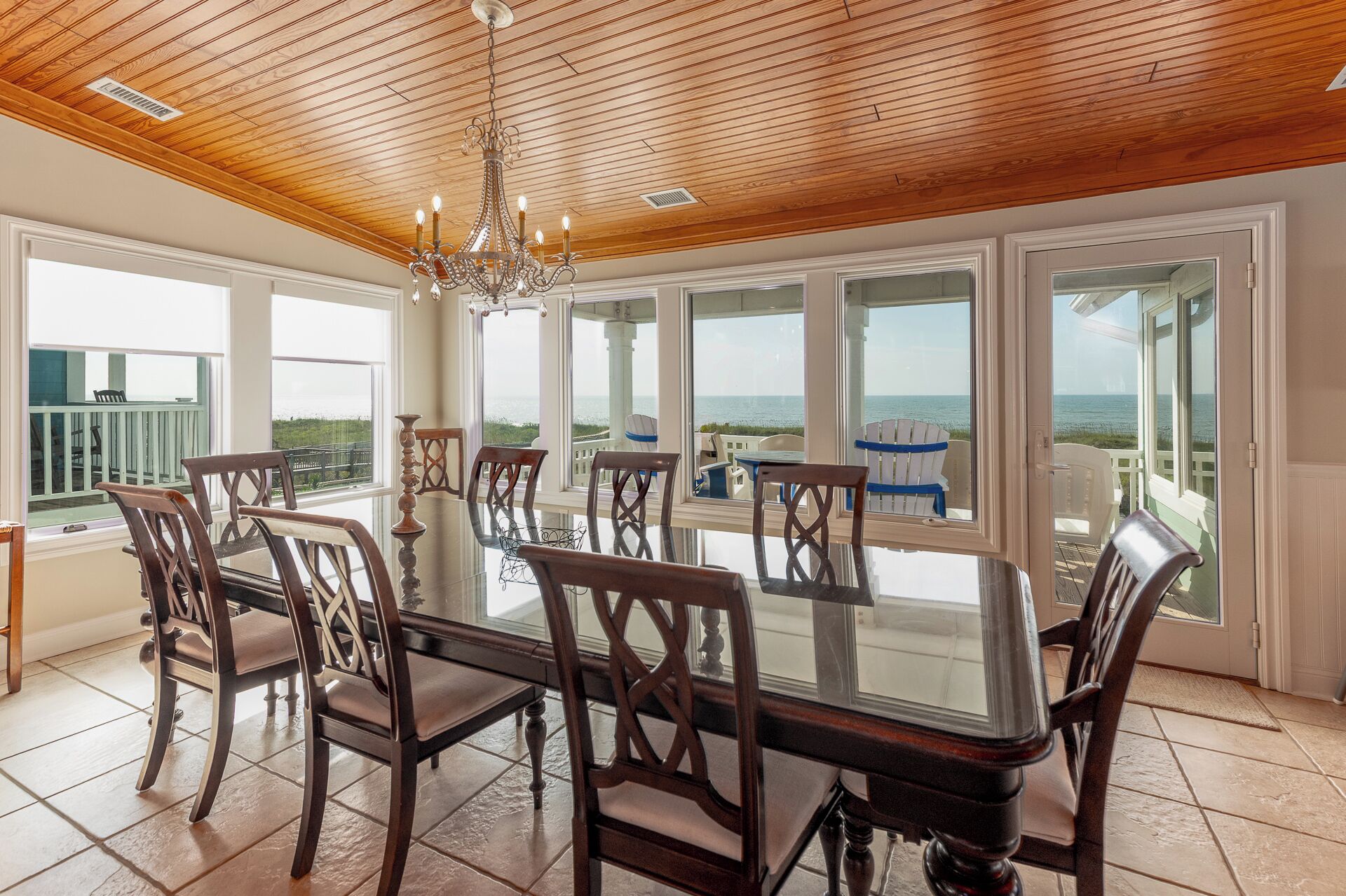 Un comedor con una mesa grande y sillas, ventanas amplias con vistas al océano y techo de madera.