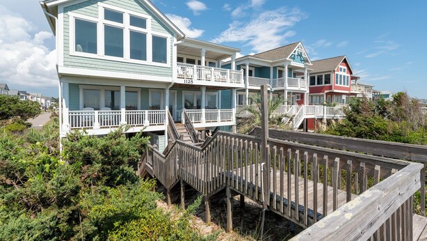 A beachfront property with a wooden deck leading to a house with multiple balconies and a covered porch.