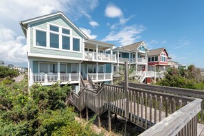Una propiedad frente a la playa con una terraza de madera que conduce a una casa con varios balcones y un porche cubierto.