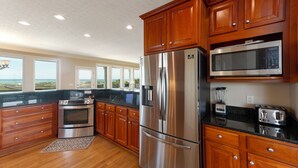 A modern kitchen with wooden cabinets, stainless steel appliances, and a view of the beach. - Hobbs Realty - "That's It II" an amazing oceanfront home with lovely views, pool, and an elevator. (Holden Beach)