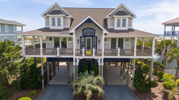 A large, two-story house with a covered front porch and a balcony. - Hobbs Realty - "That's It II" an amazing oceanfront home with lovely views, pool, and an elevator. (Holden Beach)