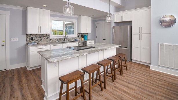 Una cocina moderna con armarios blancos, una isla de mármol, taburetes de madera e iluminación colgante.