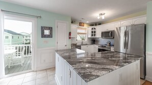 A kitchen with white cabinets, a granite island, stainless steel appliances, and a view of a balcony.