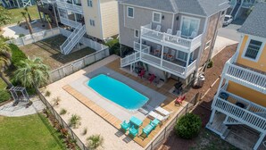 A two-story house with a swimming pool, outdoor seating, and a fenced deck.