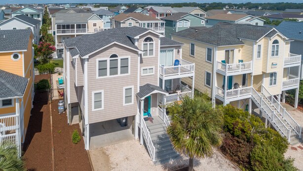 A coastal residential area with multiple two-story houses featuring balconies, a small driveway, and a sandy area in front.