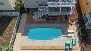 A two-story house with a swimming pool, a deck with lounge chairs, and a fenced yard.