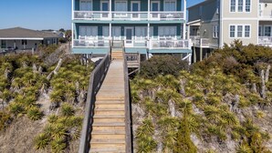 A two-story beachfront house with a wooden deck leading to the entrance. - Hobbs Realty - Oceanfront Dog Friendly w/Private Pool & EV Charger (Holden Beach)