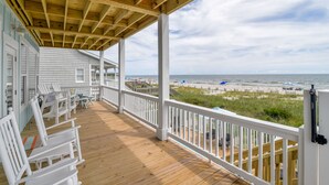 A wooden deck with white railings overlooking a beach.