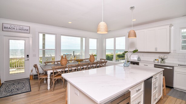 A spacious kitchen with a large island, white cabinetry, and a view of the beach.