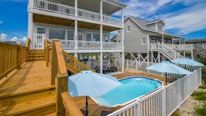A two-story house with a wooden deck, a swimming pool, and a covered patio area.