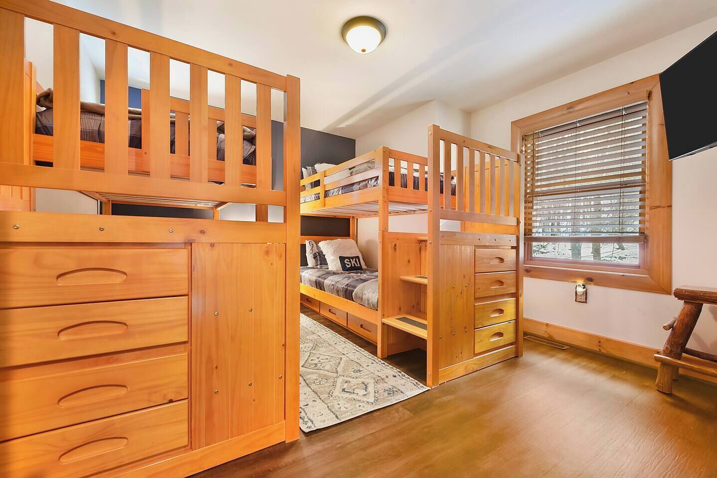Une chambre avec un lit superposé, des meubles en bois et une fenêtre avec des stores.