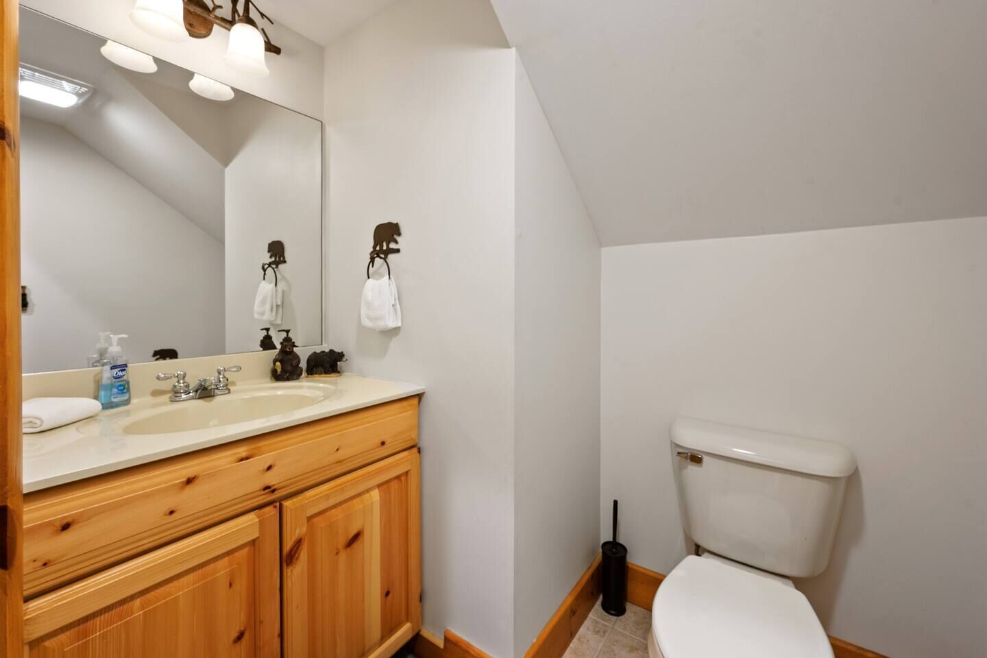 Een badkamer met een houten wastafelmeubel, een wastafel, een spiegel, een toilet en een bezem.