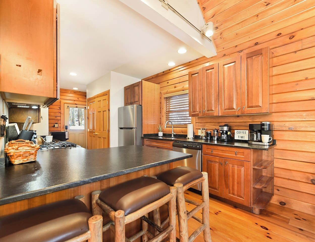 Une cuisine moderne avec des meubles en bois, un îlot central doté de tabourets, des appareils en acier inoxydable et un coin café.