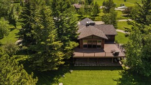 Une maison dotée d’une grande terrasse, entourée d’une forêt dense et ayant une chaîne de montagnes en toile de fond.