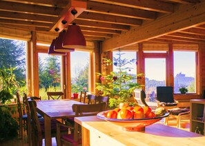 L’intérieur d’un chalet en bois, avec une table à manger, des chaises, une grande fenêtre et un saladier rempli de fruits.