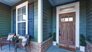 A house with a front porch, two wicker chairs with cushions, a small potted plant, and a wooden door. - Manassas House 4 BDR  Patio Firepit (Tallahassee)