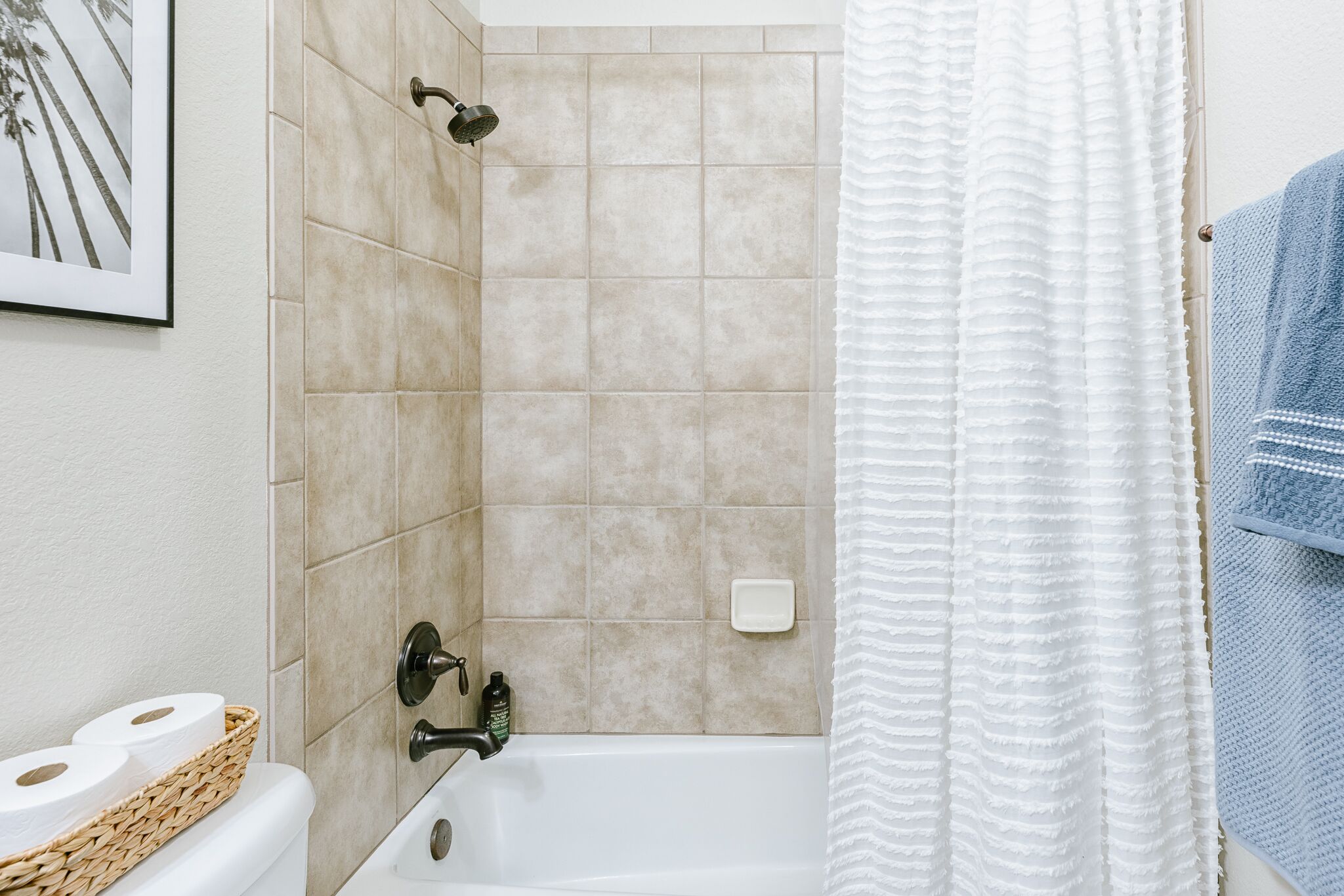 Een badkamer met een badkuip, douchekop, handdoekhouder en een ingelijst foto aan de muur.