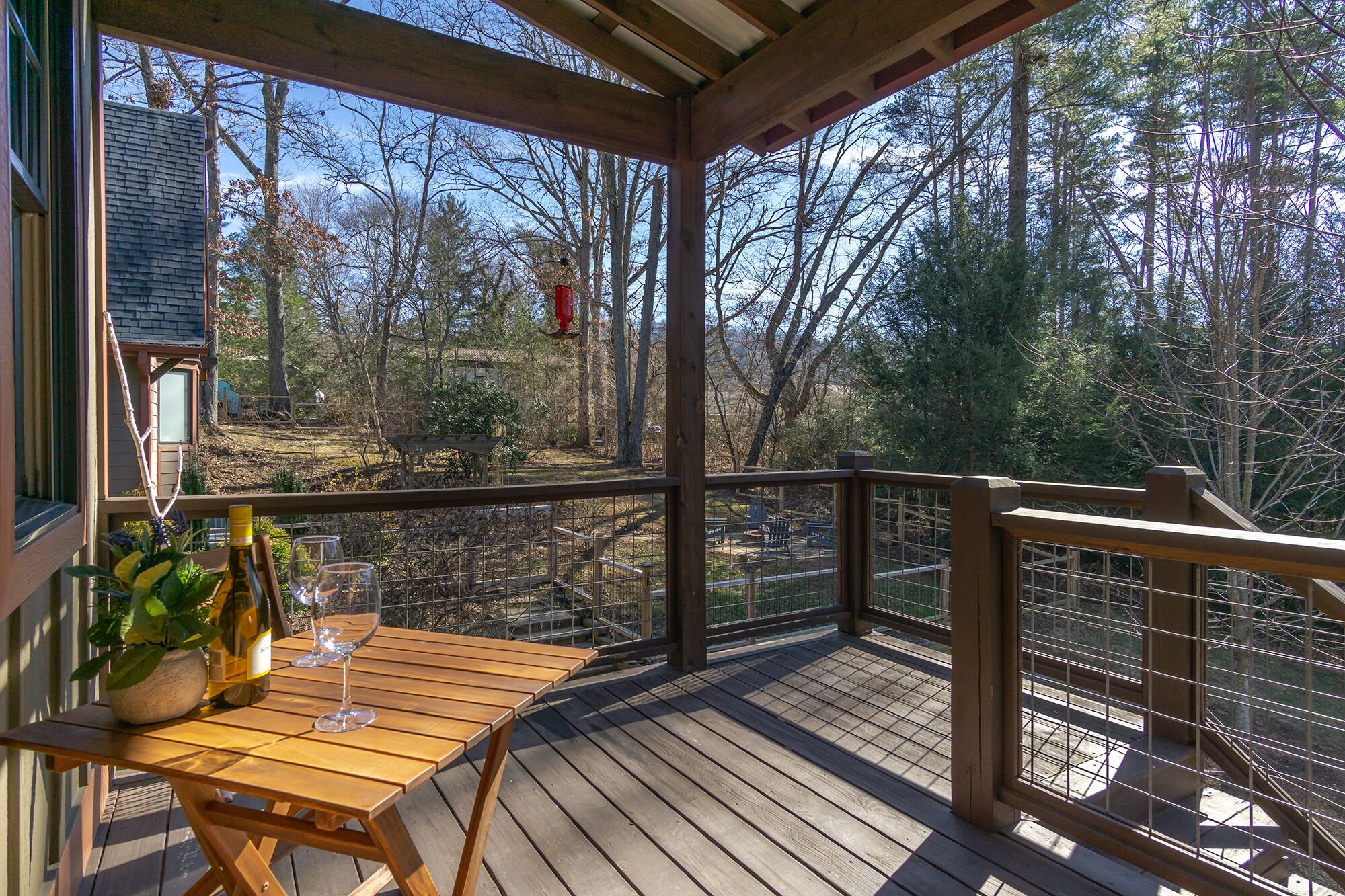 A wooden deck with a table and chairs, overlooking a forested area.