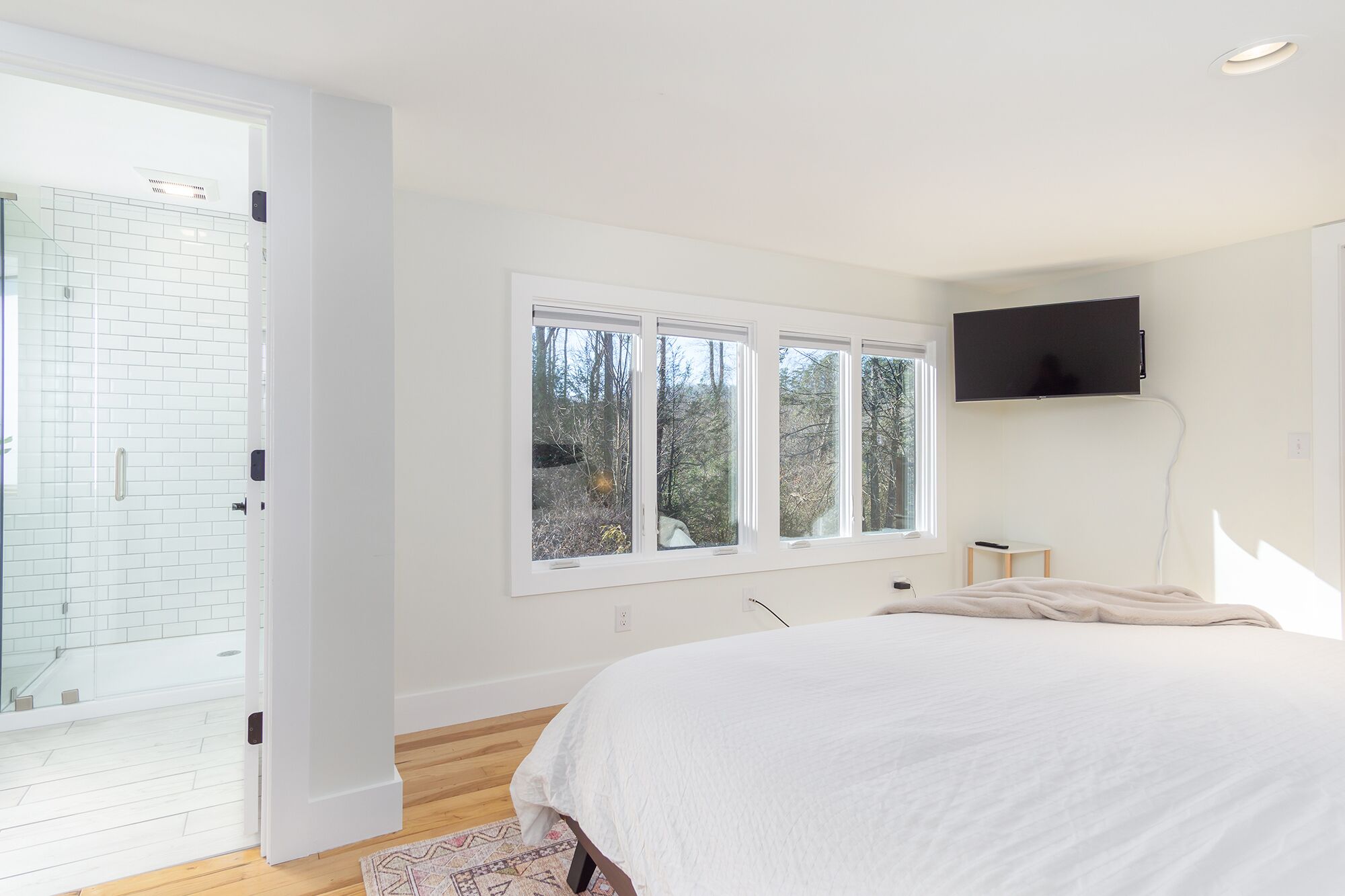 Una camera da letto con un letto grande, una TV fissata al muro e una finestra vista alberi.
