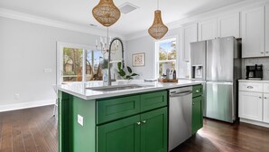 Une cuisine moderne avec des meubles de couleur verte, des appareils en acier inoxydable et des luminaires suspendus.