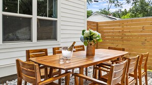 Une table de patio en bois, des chaises, un vase rempli de fleurs et une bouteille de champagne.