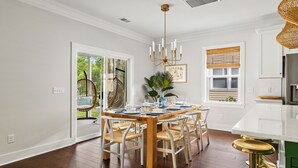 Un coin repas avec une table en bois, des chaises blanches et un lustre.