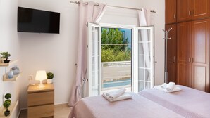 Een slaapkamer met een televisie, bedlampje, raam met gordijnen, een bed met handdoeken, een houten kledingkast en een kleine plant op een nachtkastje.