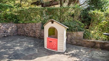 A small, stone-walled playhouse with a red mailbox, surrounded by greenery.