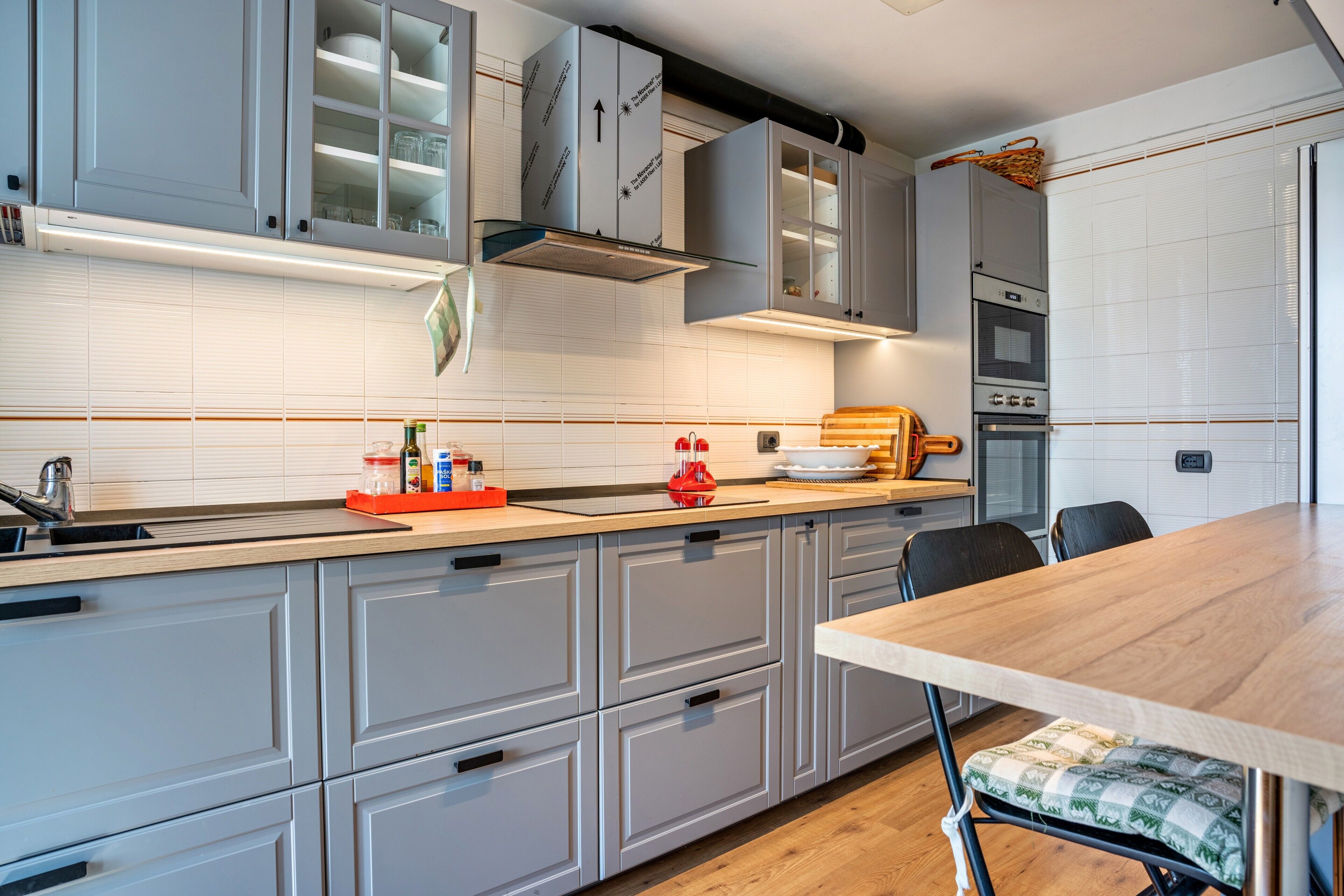 Une cuisine moderne avec des meubles gris, un plan de travail en bois et une table à manger avec un banc.