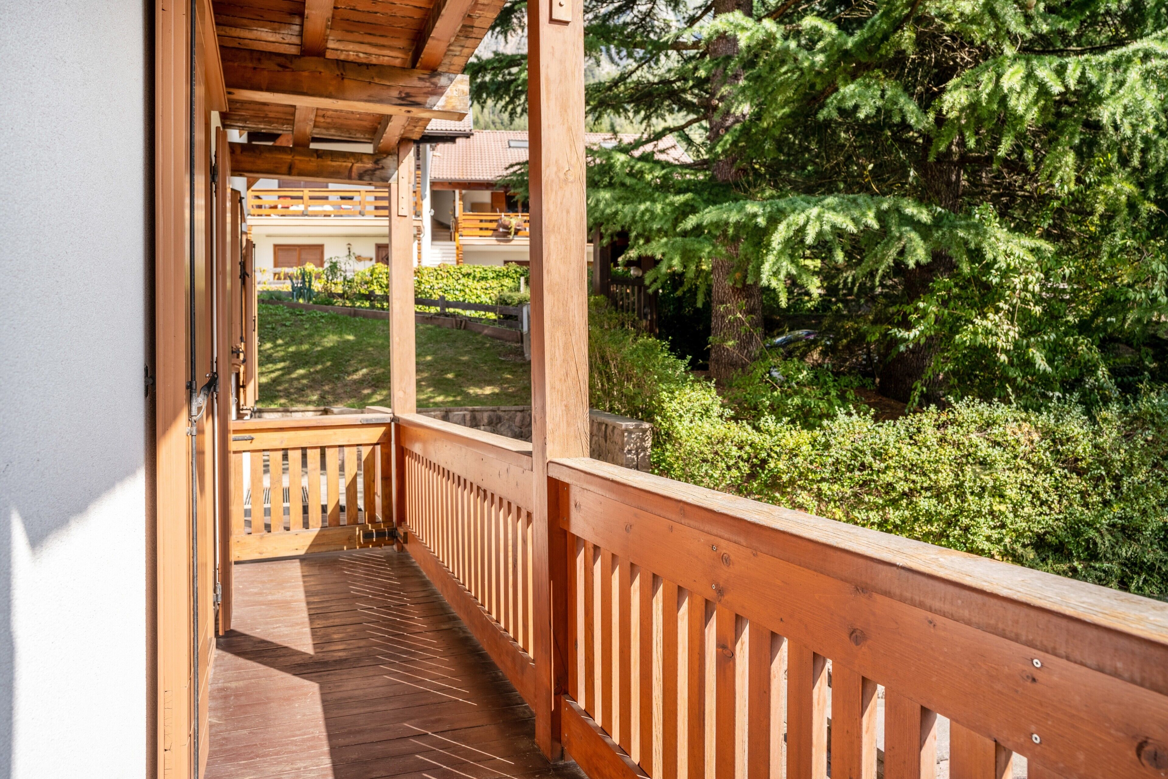 Ein hölzerner Balkon mit Blick auf einen Garten und ein Gebäude im Hintergrund.