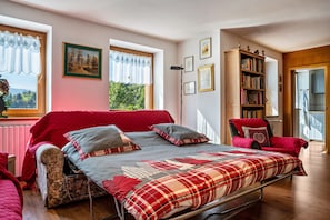 A bedroom with a bed, a chair, a bookshelf, and a window with curtains. - Holiday Home 'Magda' with Mountain View, Private Garden and Balcony (Tesero Tn)