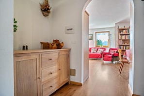 A wooden cabinet with drawers, a red sofa, and a bookshelf in a room with wooden flooring and white walls. - Holiday Home 'Magda' with Mountain View, Private Garden and Balcony (Tesero Tn)