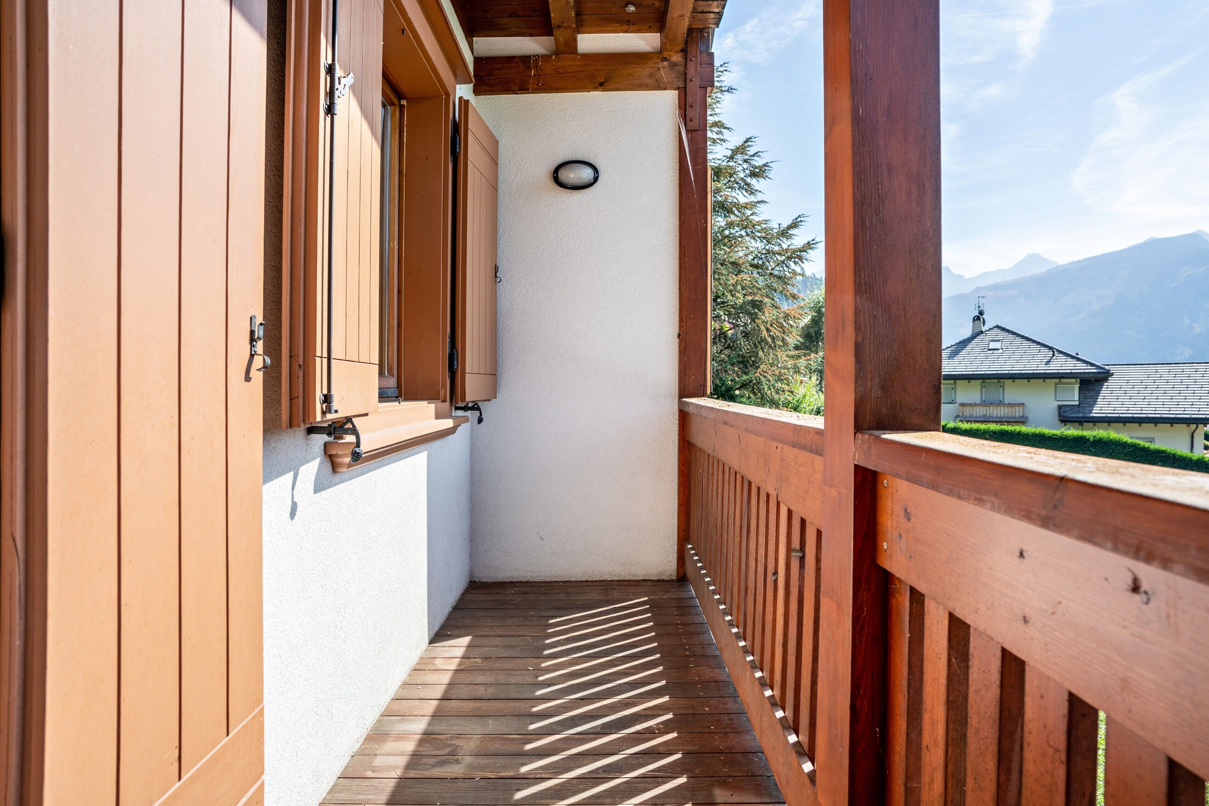 Een smal balkon met houten leuningen, een witte muur en een uitzicht op bergen op de achtergrond.
