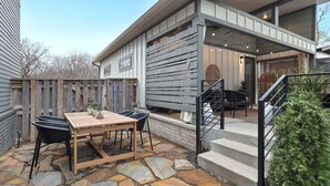 A patio with a wooden table and chairs, a stone floor, and a staircase leading to an upper level.