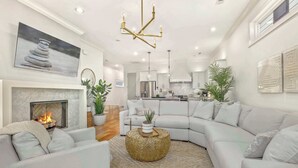 A modern living room with a fireplace, white sofas, a round coffee table, and a kitchen in the background.