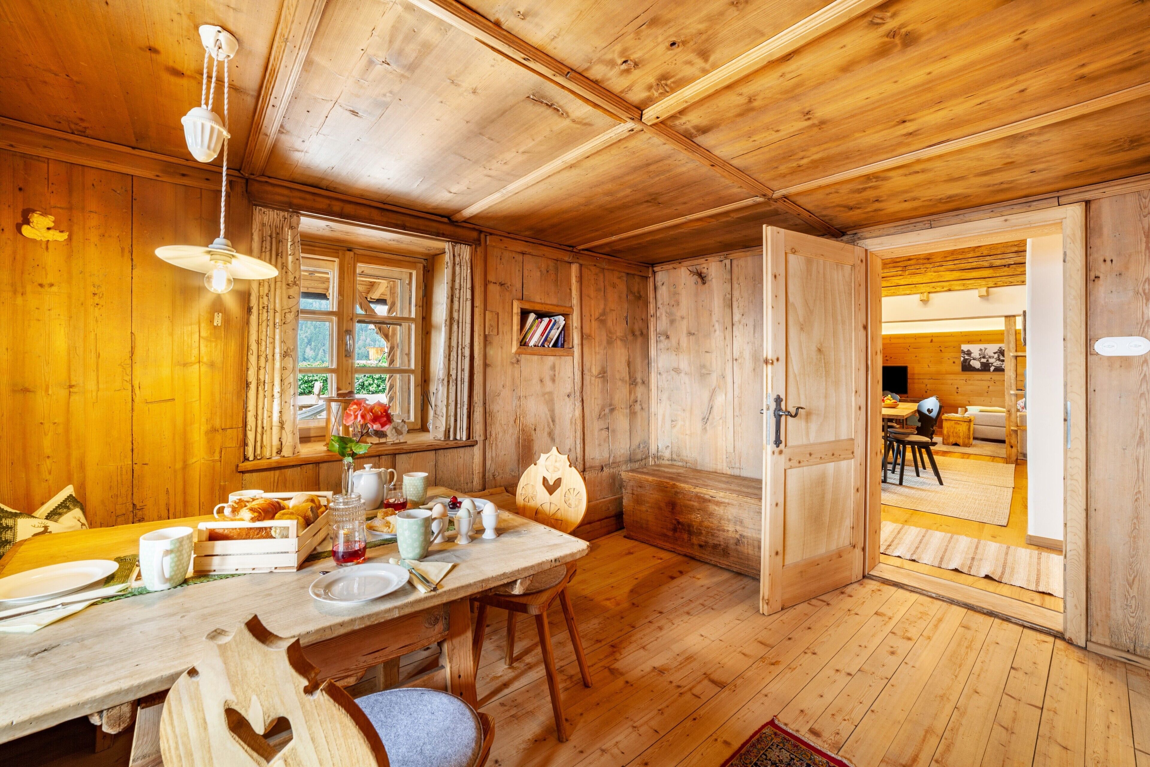 Ein Holzinterieur mit einem Esstisch, Stühlen, einer Pendelleuchte und einem Bücherregal.
