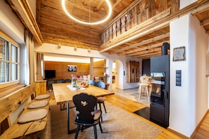 A wooden interior with a dining table, chairs, a bench, a refrigerator, and a television.