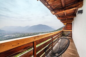 A balcony with a wooden railing, a black chair, and a view of mountains and a valley. - Holiday Home 'Mutlechnerhof' with Mountain View, Private Terrace and Wi-Fi (Caines)